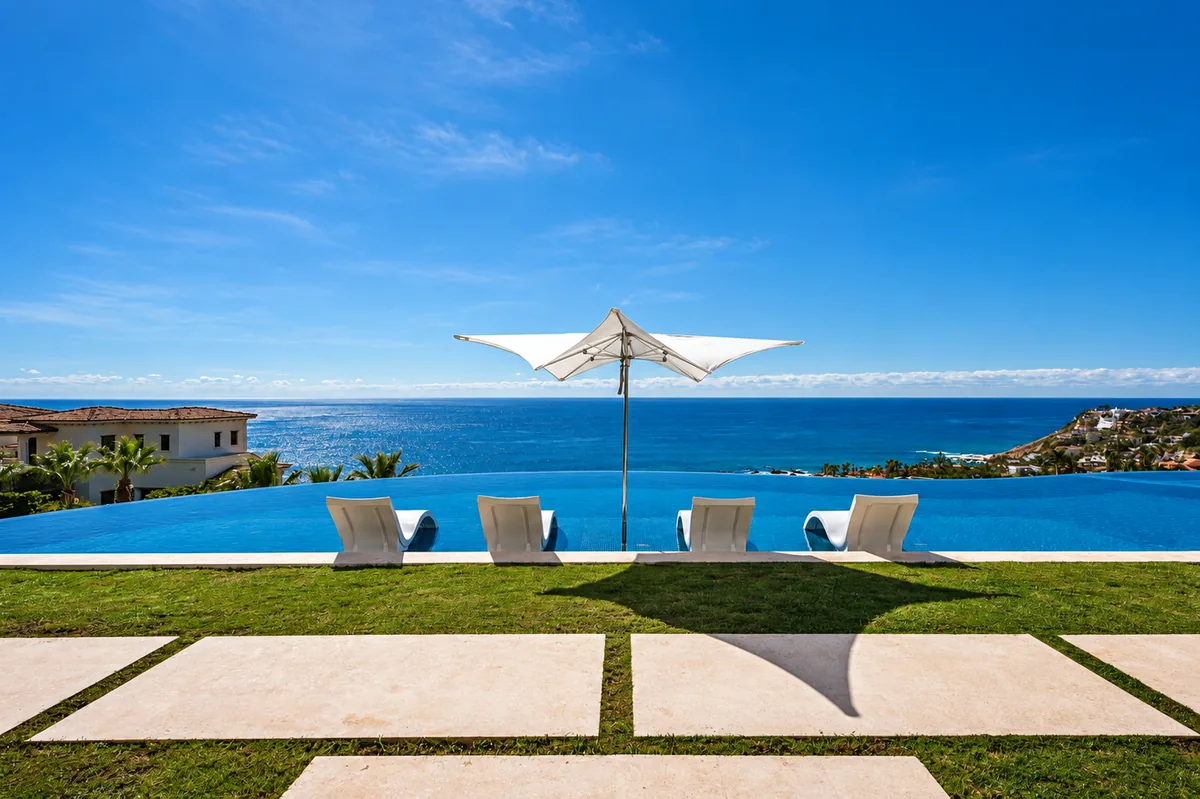 An infinity pool with loungers and a parasol overlooking the Cabo coastline